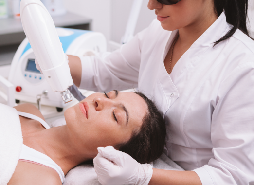 A woman lays peacefully on the treatment table as a provider treats her facial skin with an energy device.
